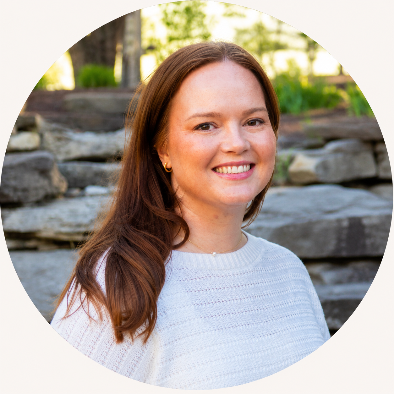 Ashton, founder of ASHTON RENÉE, smiling outdoors in a white sweater and gold earrings
