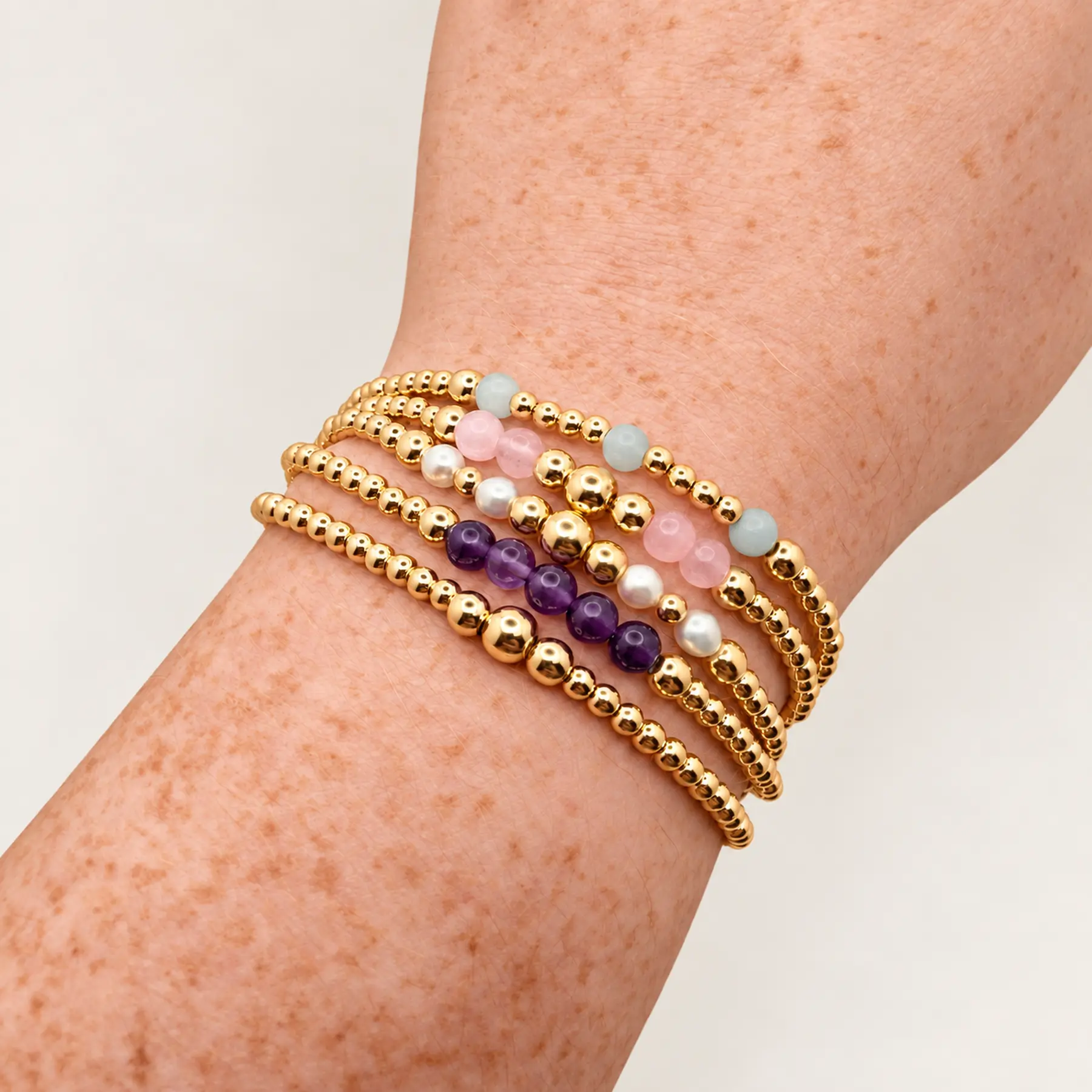 Five ASHTON RENÉE bracelets stacked on a wrist, featuring polished gold-filled beads, amethyst, freshwater pearls, rose quartz and aquamarine