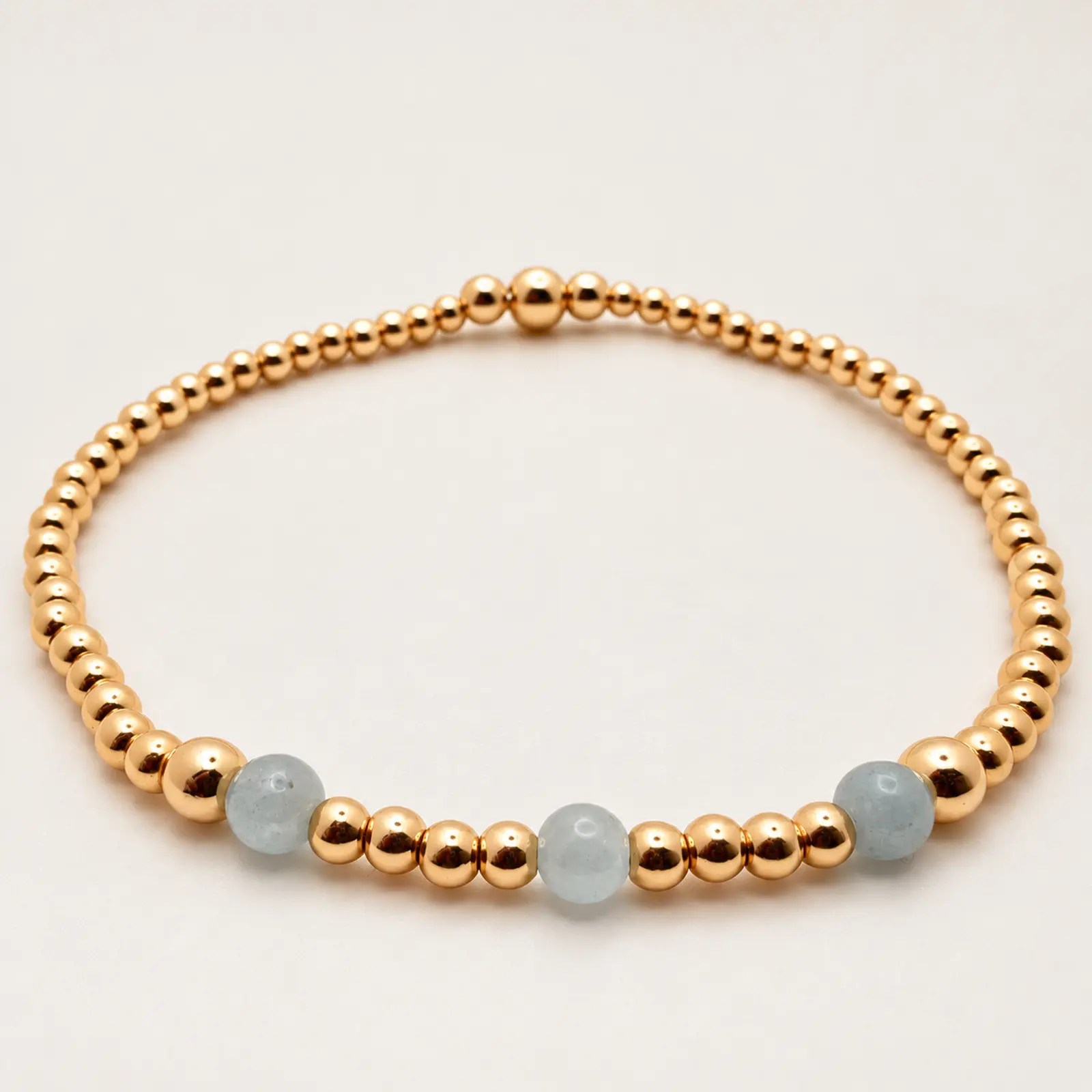 The Chelsea stretch bracelet arranged in a circle, with three pale blue aquamarine beads and polished 14K gold-filled beads
