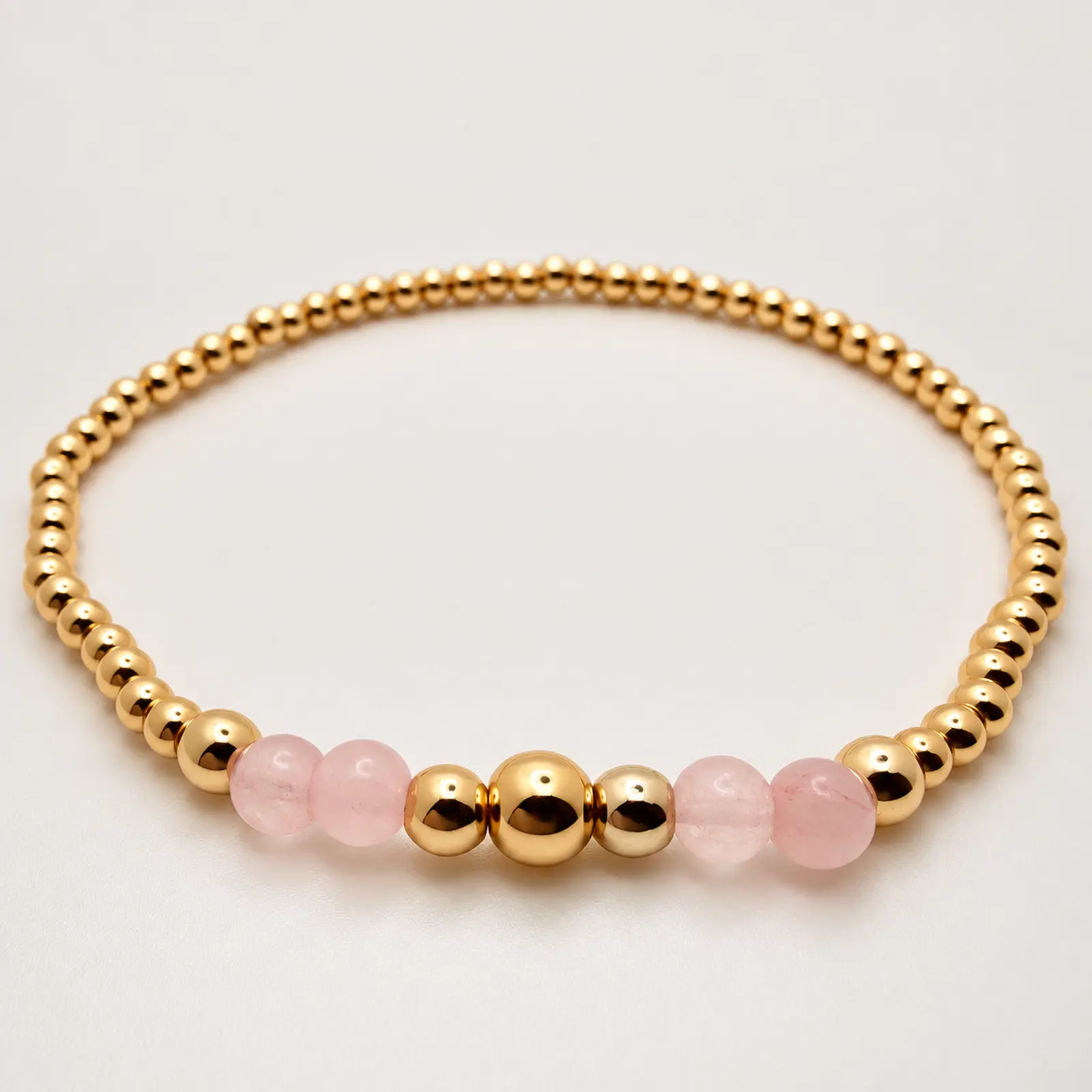 The Samantha stretch bracelet arranged in a circle, with four pale pink rose quartz beads surrounding a graduated 14K gold-filled bead center